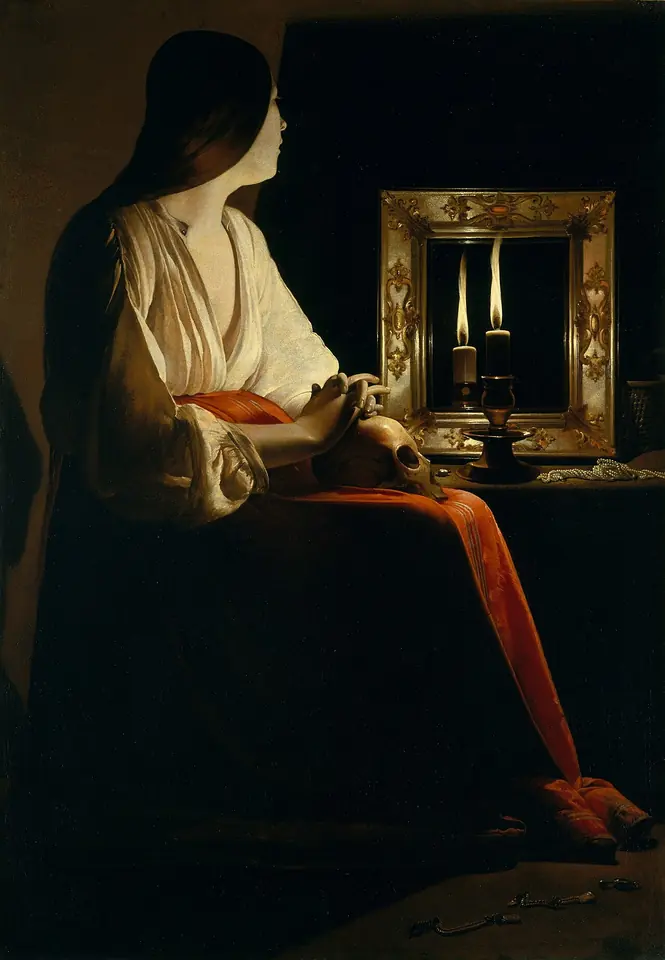 Mary Magdalene sits in a dark room in a white blouse and red skirt, one hand resting on a skull in her lap, gazing at a candle reflected in a gilded mirror