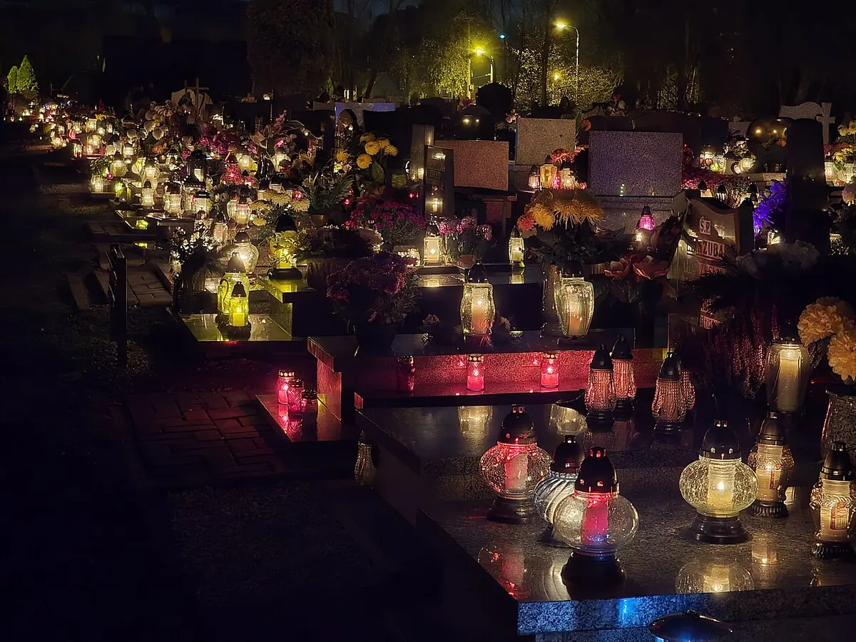 Cemetery at night with hundreds of red, white and amber candle lanterns glowing on the graves among flowers