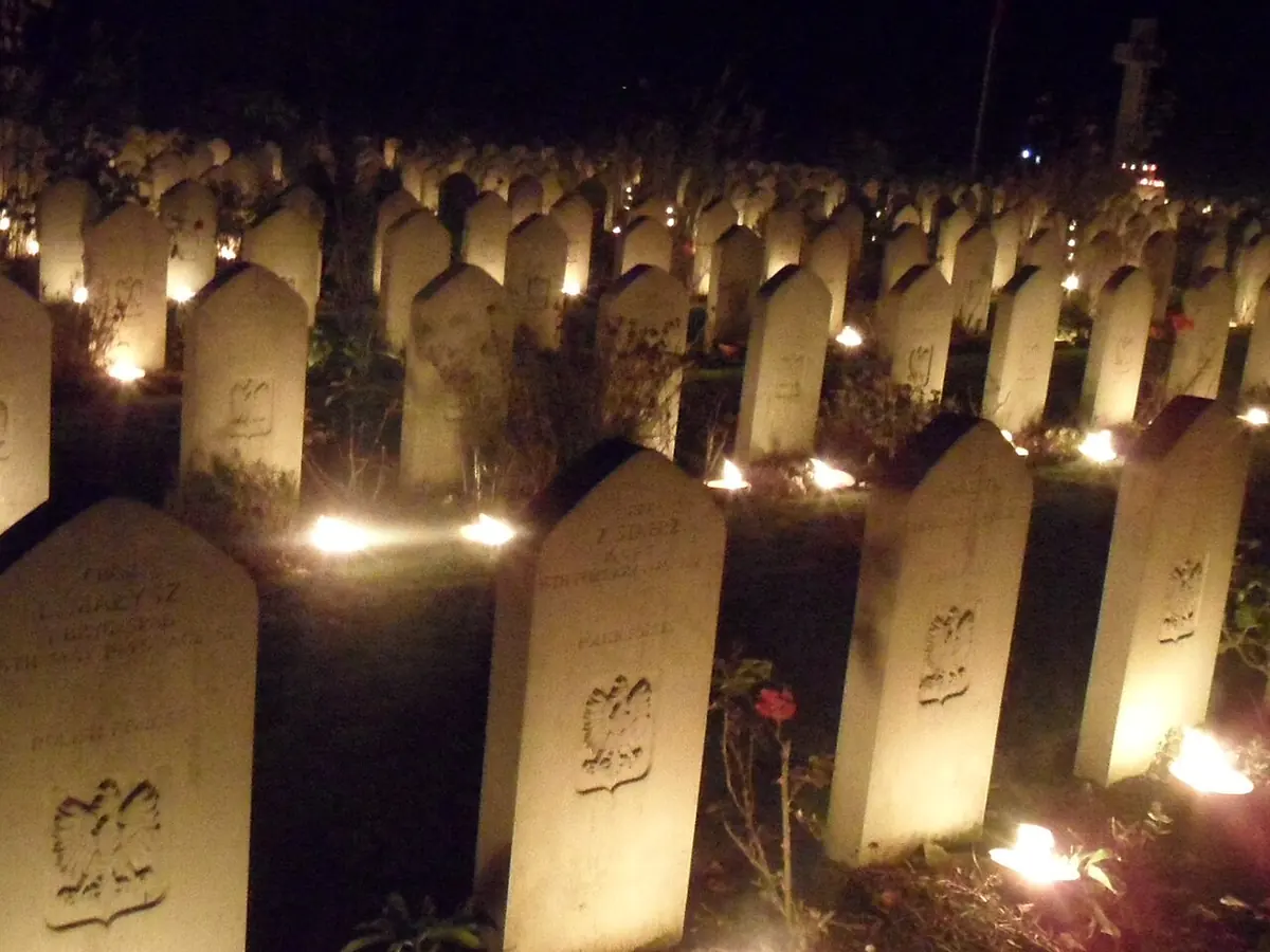Rows of white headstones in a cemetery at night, each with candles glowing at its foot