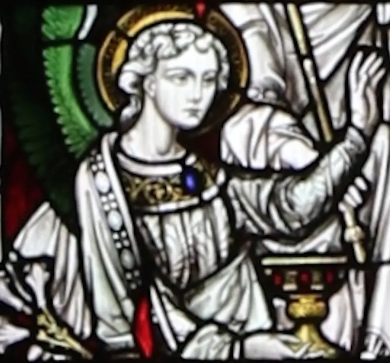 Close view of a stained-glass angel with a gold halo and a white robe, raising one hand beside a golden chalice