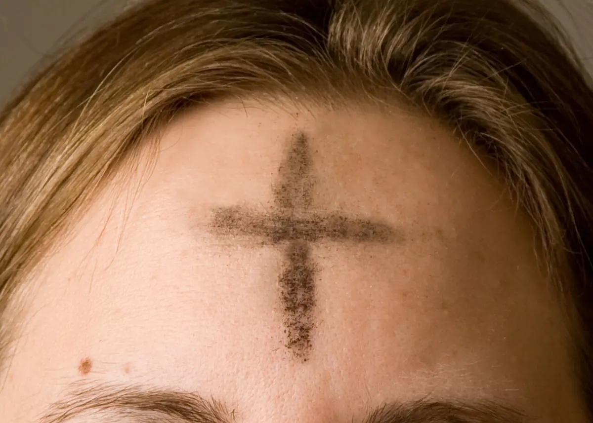 Close view of a woman's forehead marked with a dark, smudged cross of ashes