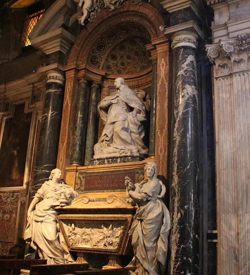 Marble papal tomb in a side chapel of a Roman church, with a kneeling statue of the pope above a sarcophagus flanked by two standing female figures, between dark marble columns
