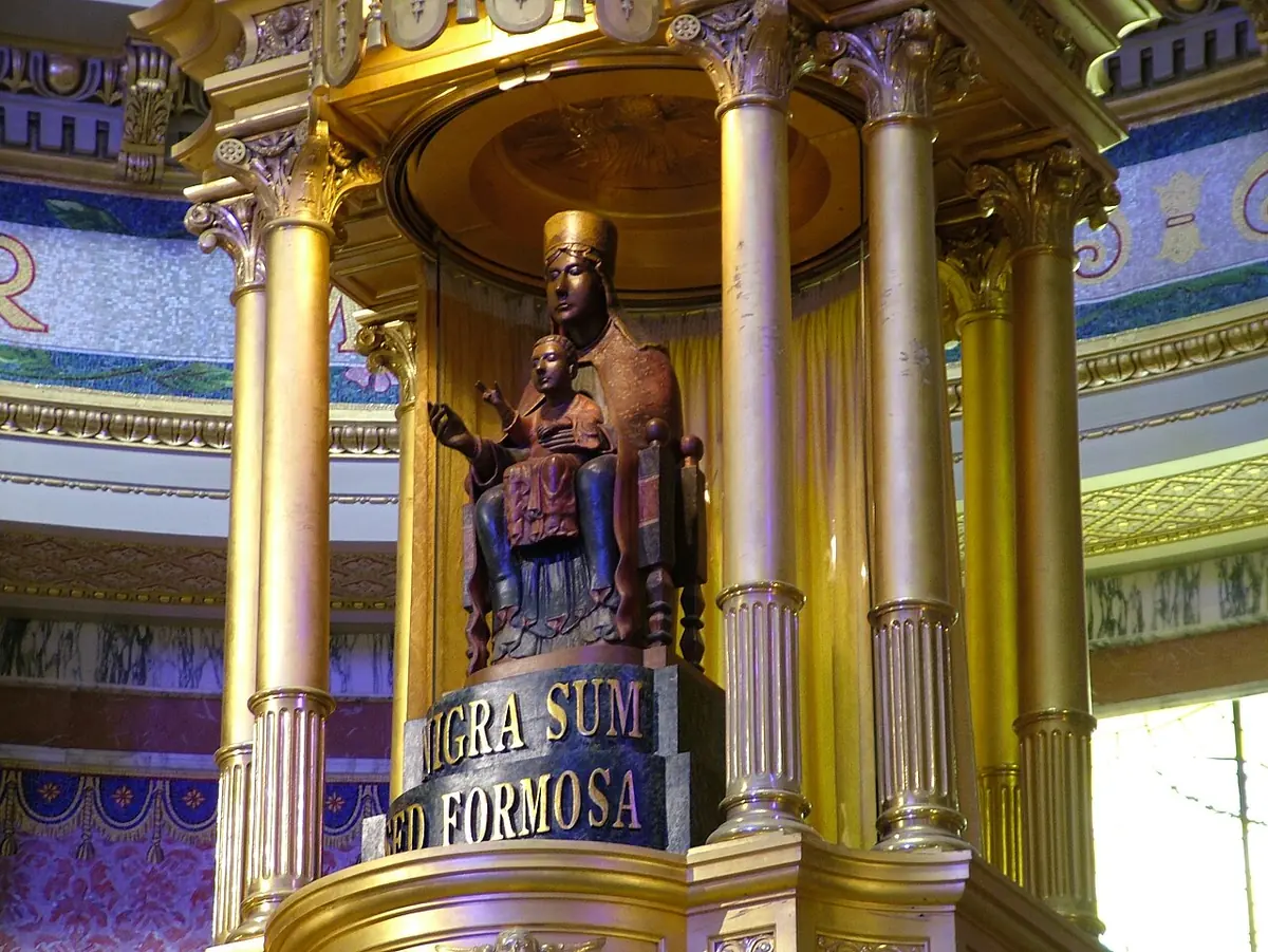 A dark seated statue of the Virgin and Child under a gilded round canopy with columns, on a base inscribed NIGRA SUM SED FORMOSA
