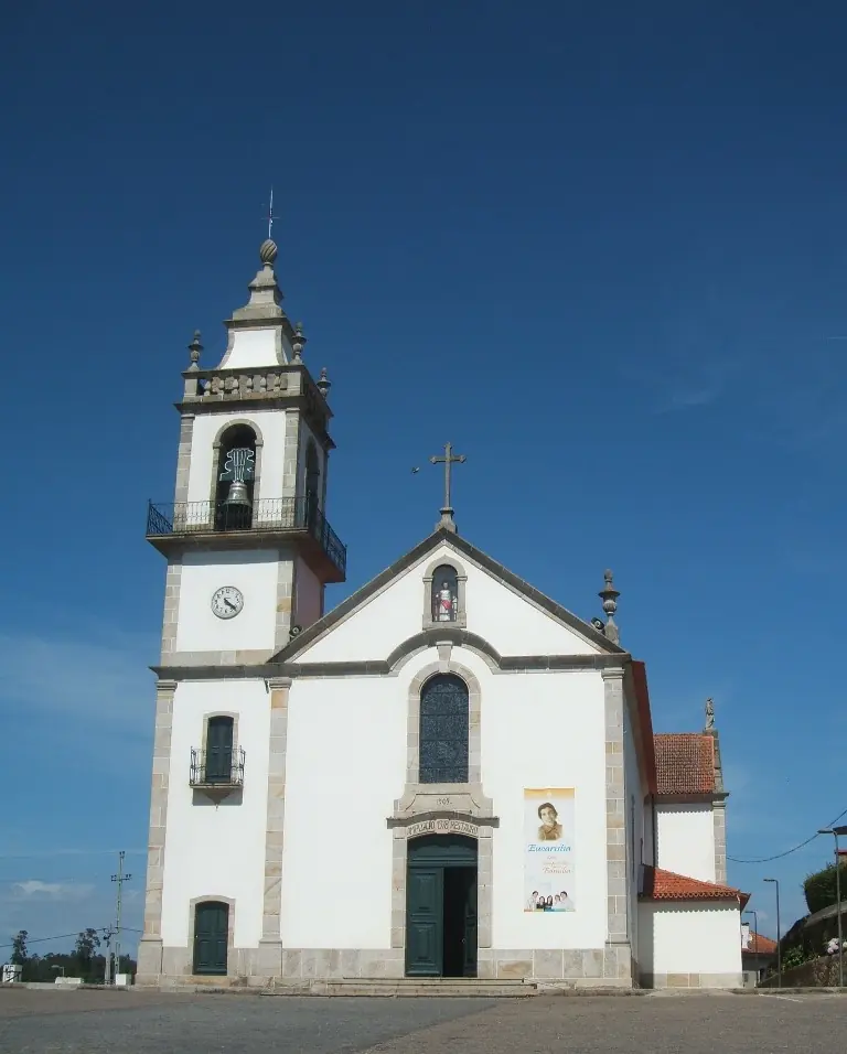A white parish church with a granite-trimmed bell tower and a cross on the gable under a deep blue sky