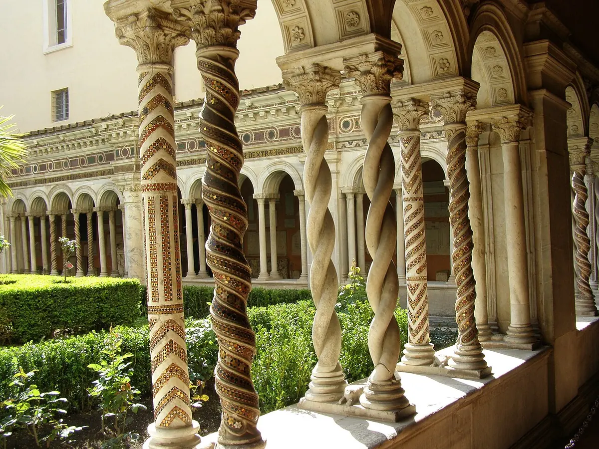 A sunny medieval cloister with rows of slender twisted and inlaid columns around a green garden