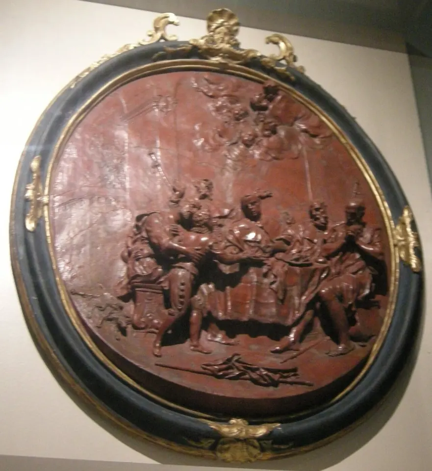 Round reddish relief in a gilded frame showing a figure handing out food to a crowd of pilgrims at a table