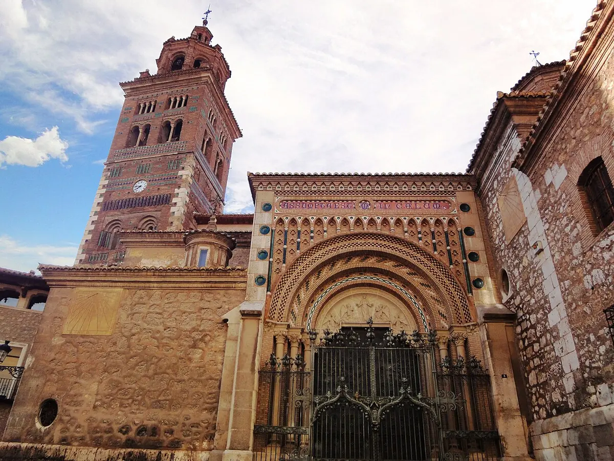 The brick Mudéjar cathedral of Teruel with its decorated bell tower and a carved doorway behind an iron gate