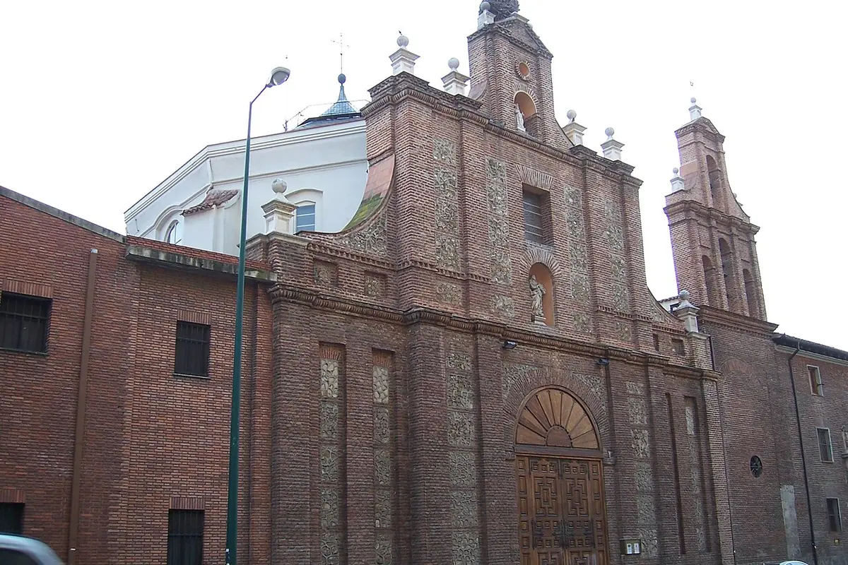 Brick Baroque church front of the English College in Valladolid, with a carved stone doorway, a small bell tower and a white dome behind