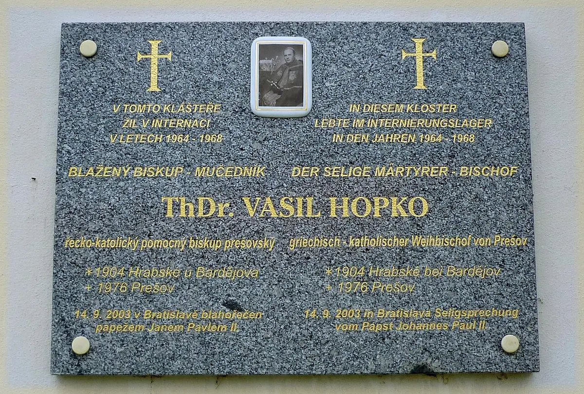 A gray granite plaque in Czech and German with two gold crosses and a small photograph, recording that Blessed Bishop Vasil' Hopko lived in internment in the monastery from 1964 to 1968