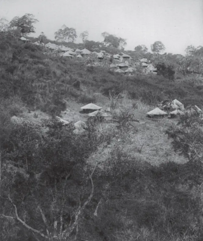 Old black-and-white photograph of round thatched huts scattered on a bushy hillside