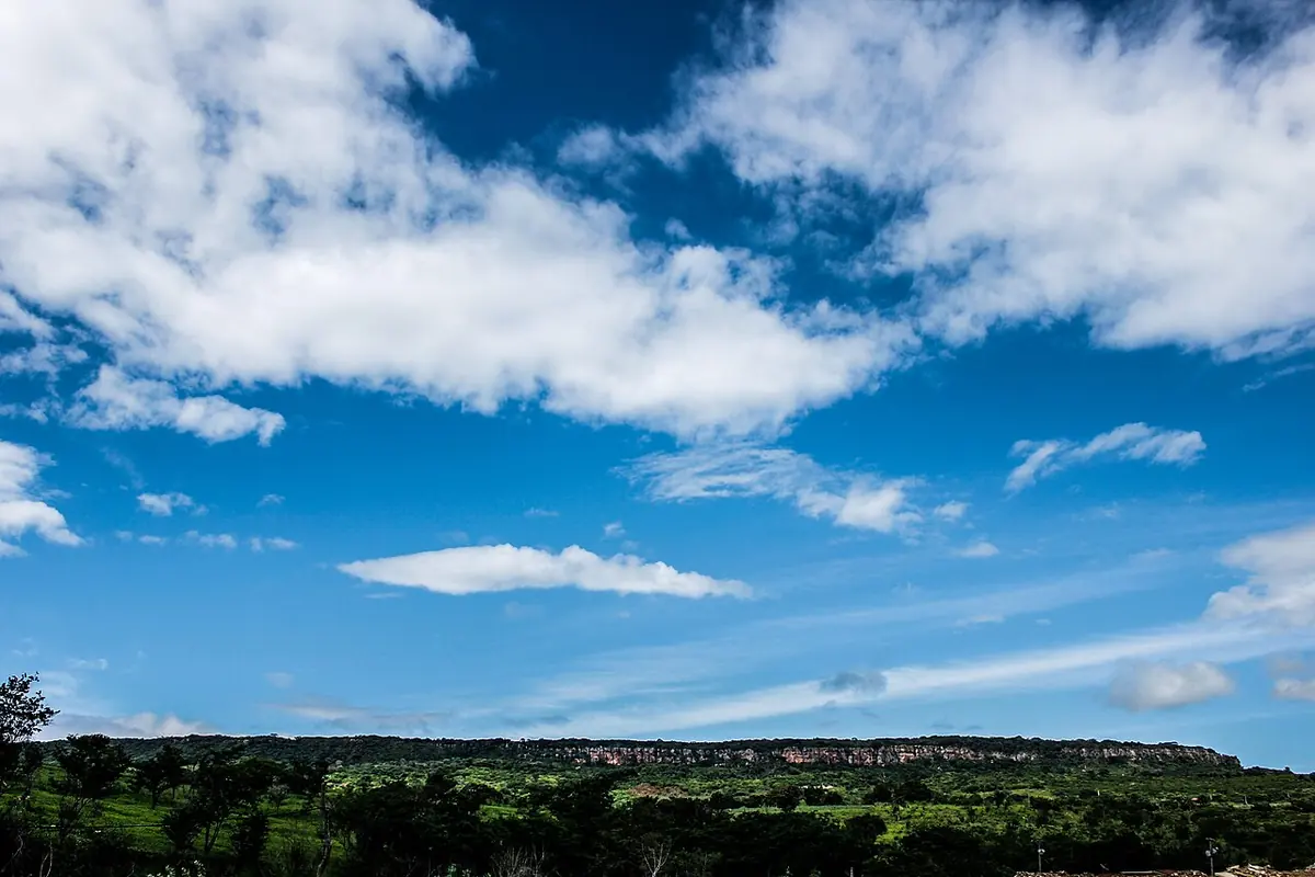A long flat-topped plateau on the horizon under a blue sky with white clouds, above green scrubland