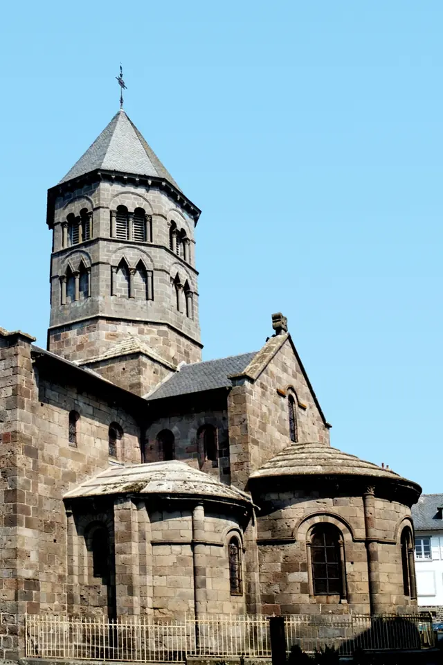 The octagonal stone bell tower and rounded east end of a dark Romanesque church against a blue sky