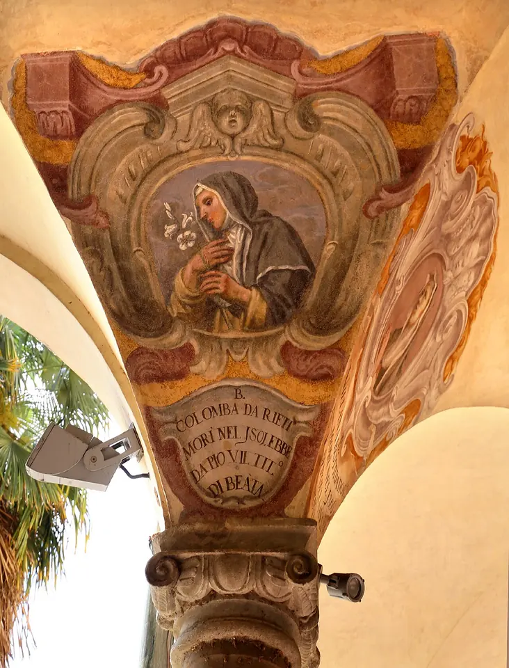 A fresco in a cloister vault showing Blessed Columba in a black veil gazing down at a lily in her hands, in a painted cartouche