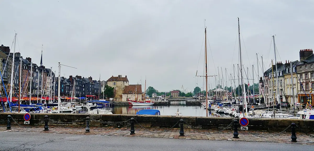 Sailboats moored in the old harbor of Honfleur, with tall narrow slate-fronted houses along the quay