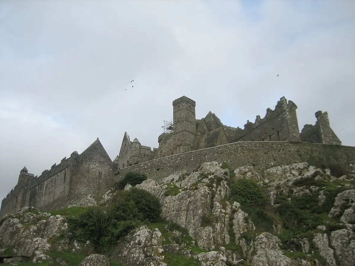 The ruined medieval cathedral and round tower of the Rock of Cashel on its limestone outcrop, seen from below under a gray sky