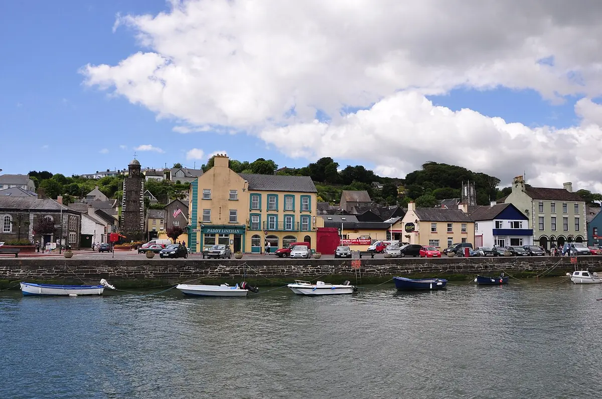Small boats moored in front of a row of colorful houses and a church tower along the harbor wall at Youghal
