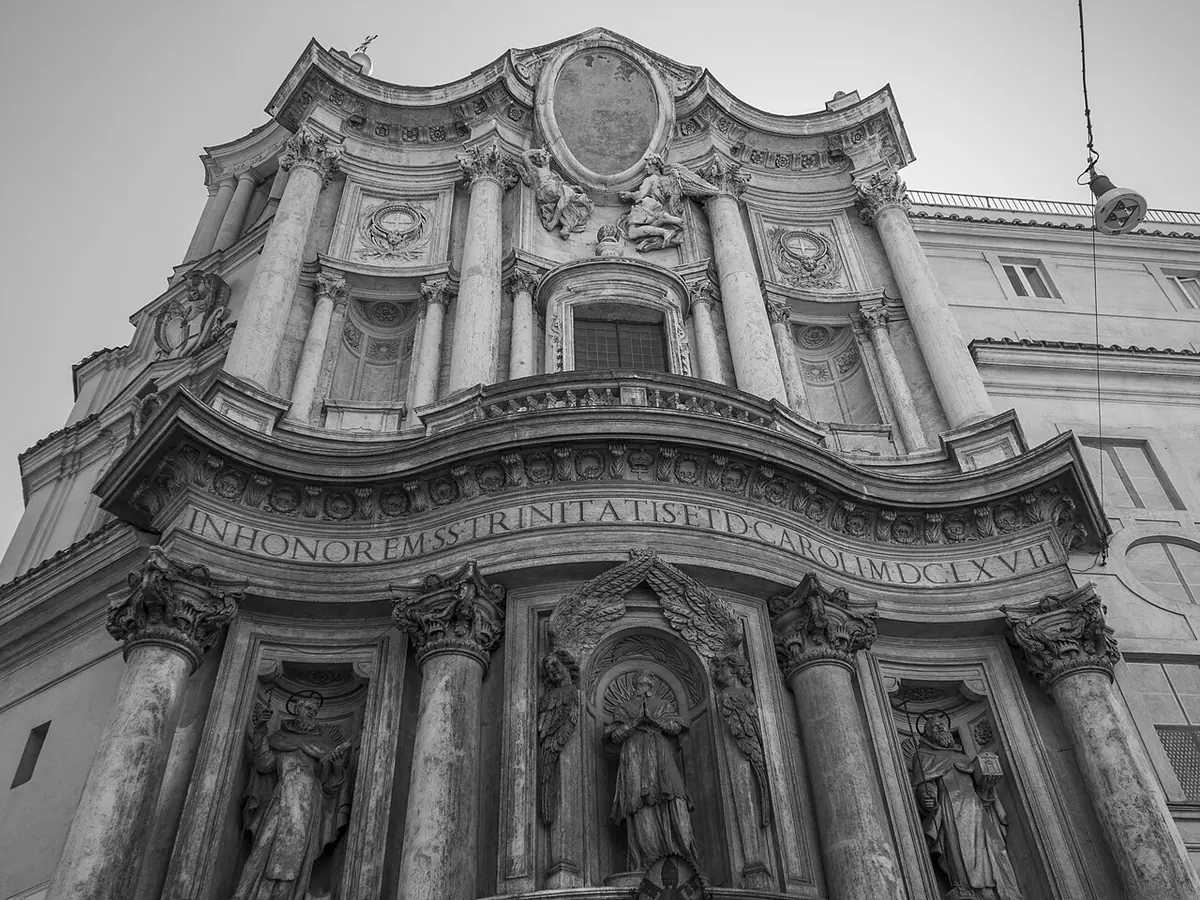 The curving Baroque stone facade of San Carlo alle Quattro Fontane in Rome, with columns, statues in niches and a carved inscription, seen from below