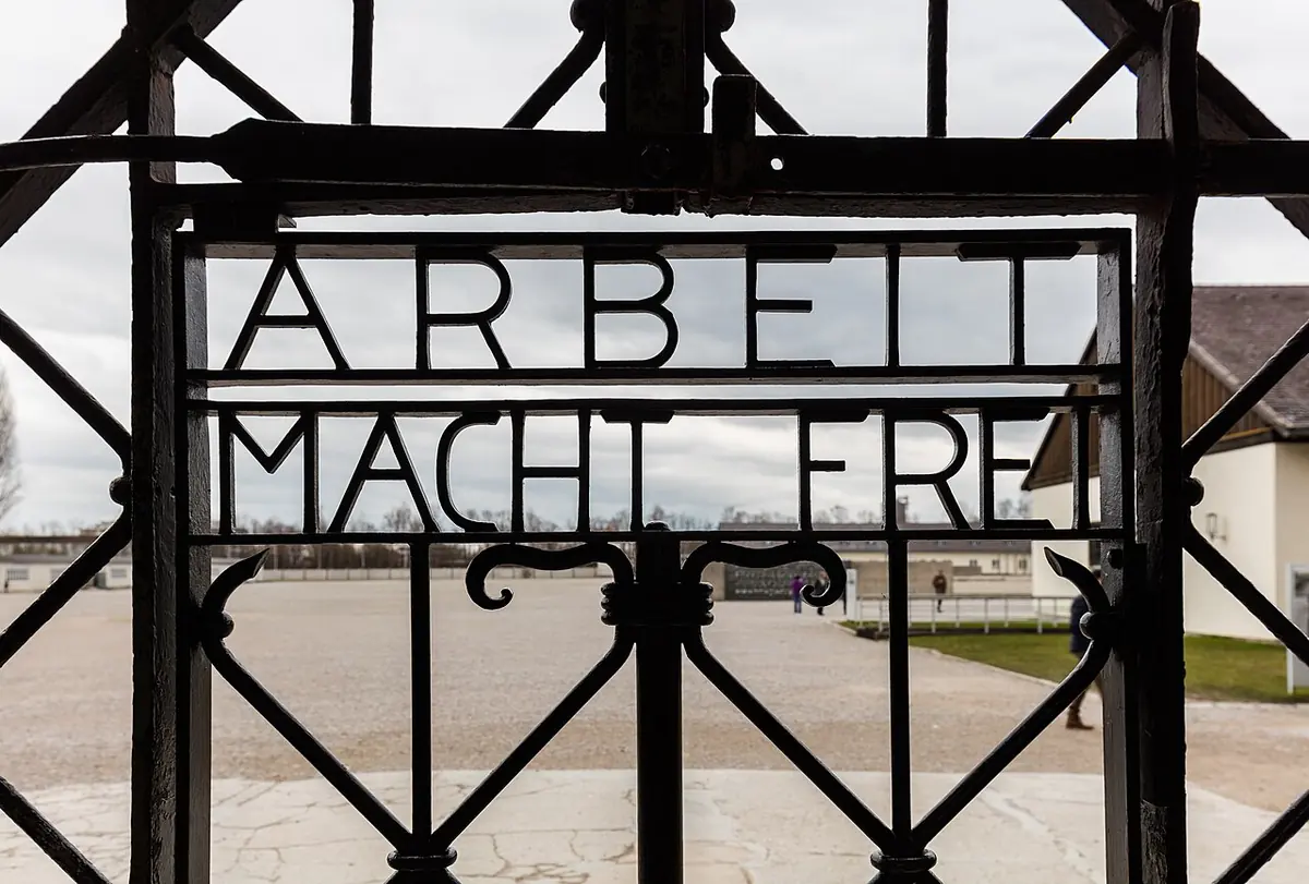 Wrought-iron gate with the words "Arbeit macht frei," looking out onto the empty parade ground of the former Dachau camp