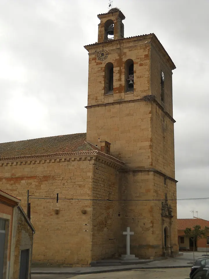 A tall square sandstone church tower with open bell arches beside the long stone nave of a village church, a stone cross in front