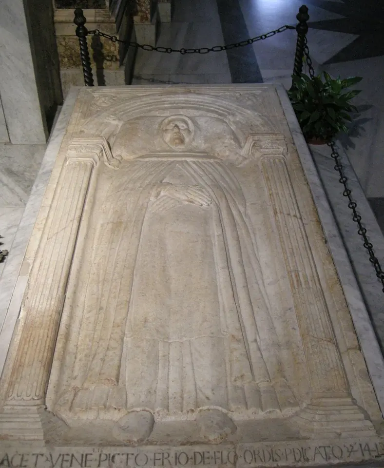 Worn marble tomb slab carved with the full-length figure of a friar in his habit lying with his hands crossed, framed by a carved arch, set in the floor behind a low rail