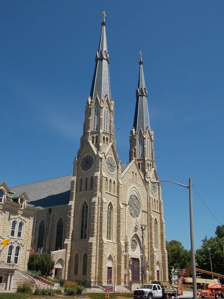 The pale stone Gothic Revival facade of St. Mary's Cathedral in Peoria with two tall spires against a blue sky
