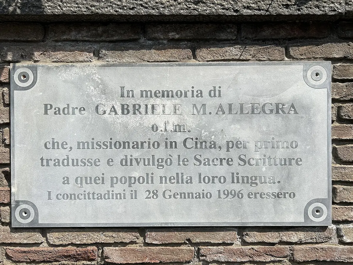 A gray stone plaque on a brick wall with an Italian inscription in memory of Father Gabriele M. Allegra, first translator of the Scriptures into Chinese