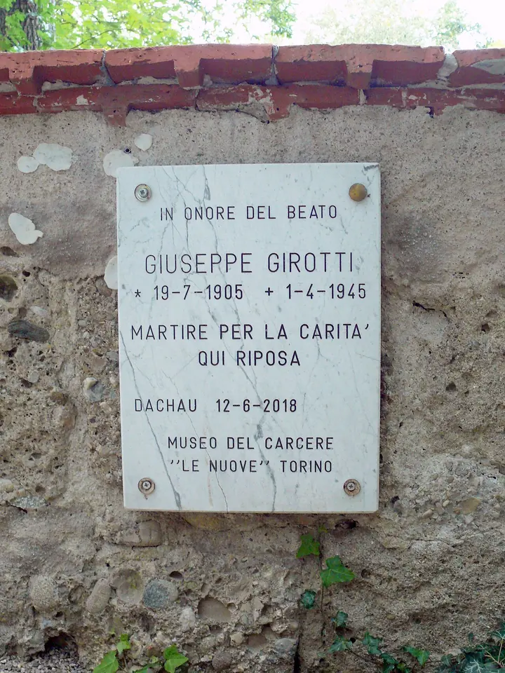 A small white marble plaque on an old stone wall reading in Italian that Blessed Giuseppe Girotti, martyr of charity, rests here
