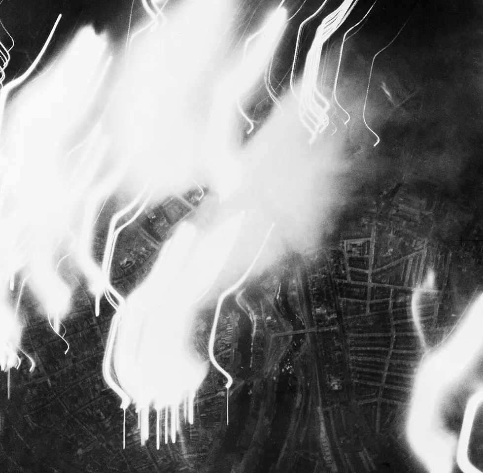 A black-and-white night aerial photograph of Lübeck with bright streaks of fire and light across the old town and the river