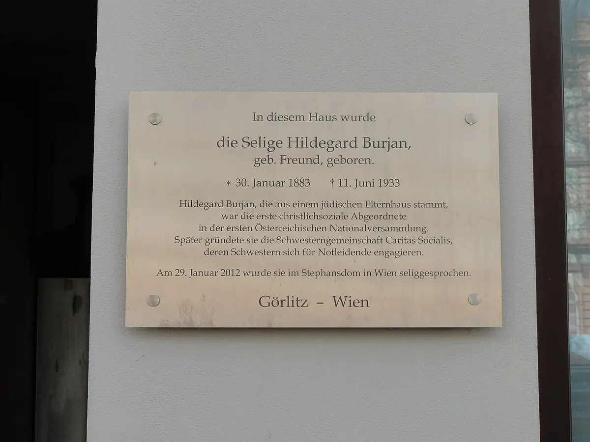 A pale wooden plaque with German text recording that Blessed Hildegard Burjan, born Freund, was born in this house on January 30, 1883, and beatified in Vienna in 2012