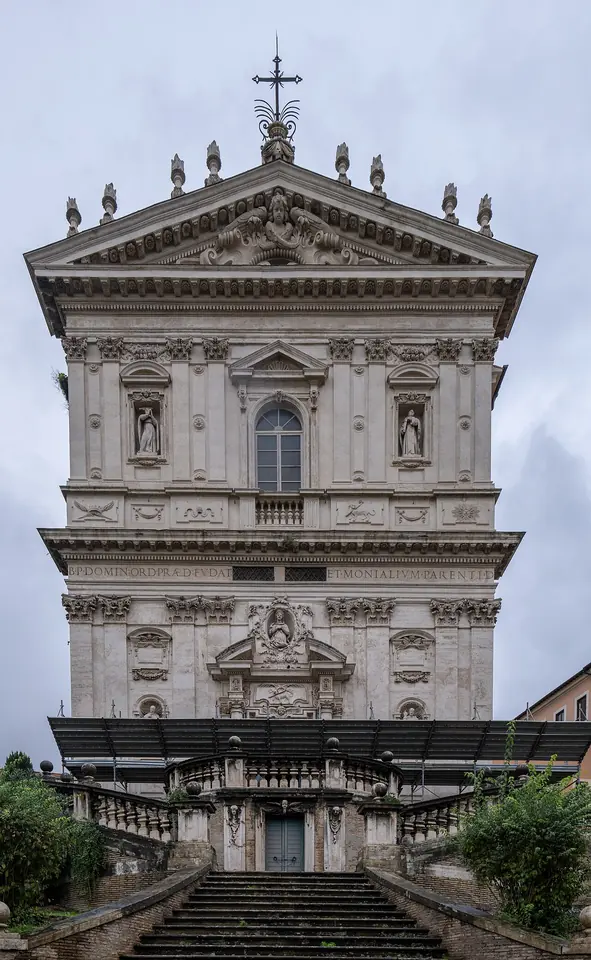 The tall Baroque facade of the church of Santi Domenico e Sisto in Rome, in pale stone with columns and statues, above a double staircase
