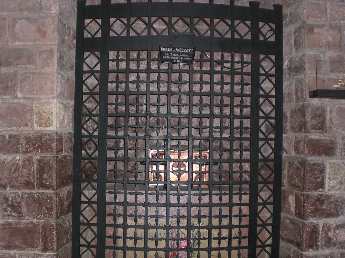 An iron grille set in a wall of red and pink stone, with a small inscription plate above it and the burial niche behind