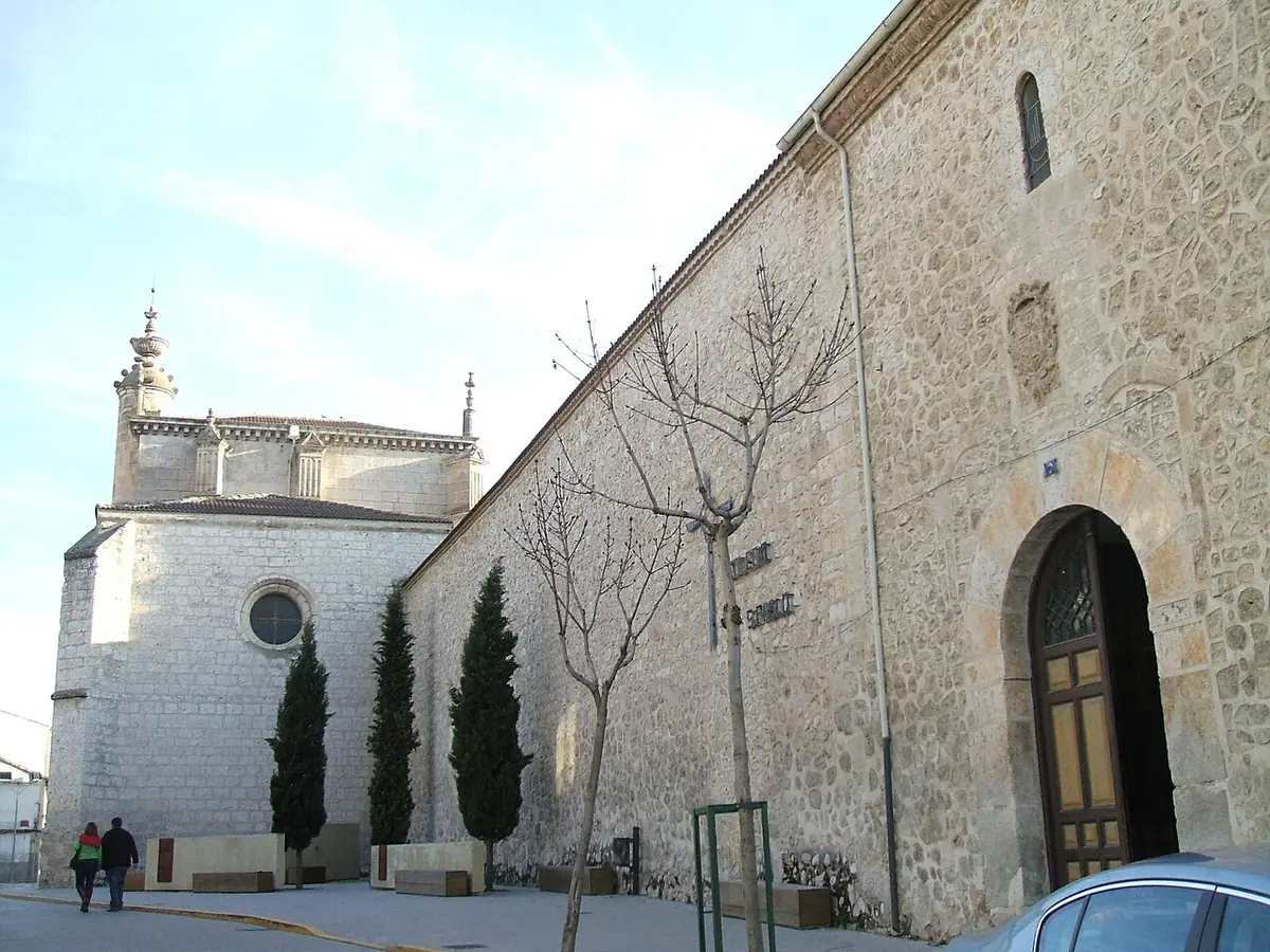 The long stone wall and white apse of the convent church of San Pablo in Peñafiel, with cypress trees along the walk