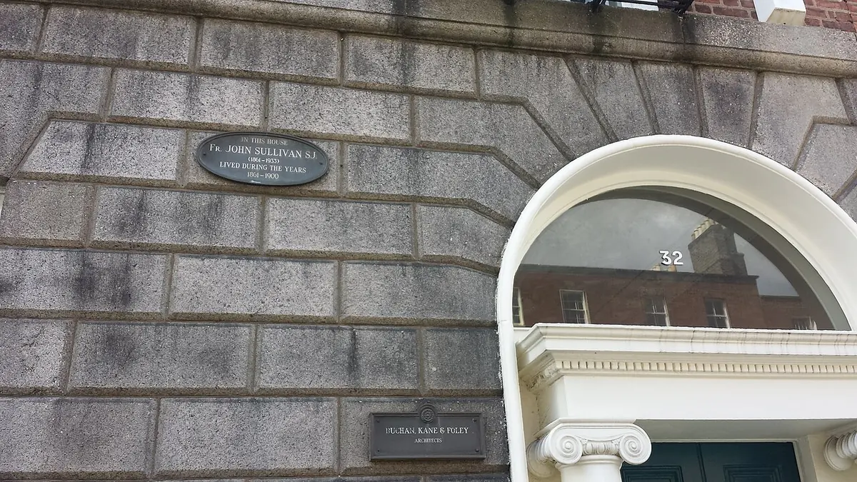 A gray granite Georgian house front with a small oval commemorative plaque beside a white fanlight doorway