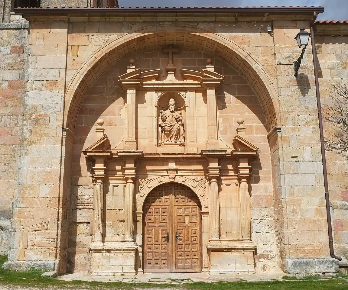 The carved sandstone portal of the village church of Hacinas, with a round arch, columns and a seated statue of a saint in a niche above the wooden doors
