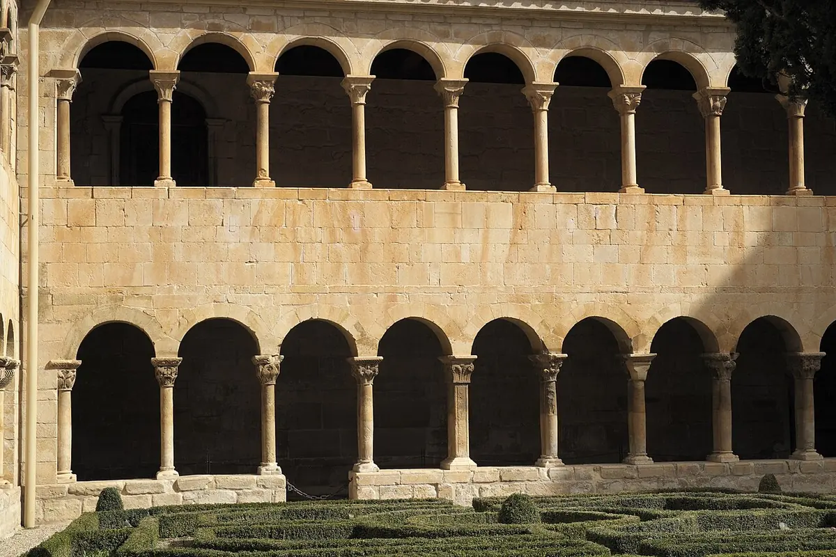 Two stories of round Romanesque arches on paired columns around the cloister garden of the Abbey of Silos, with clipped box hedges in front