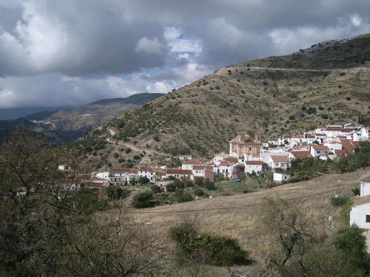A small white village with a large church spread across a dry green hillside in the mountains of Málaga