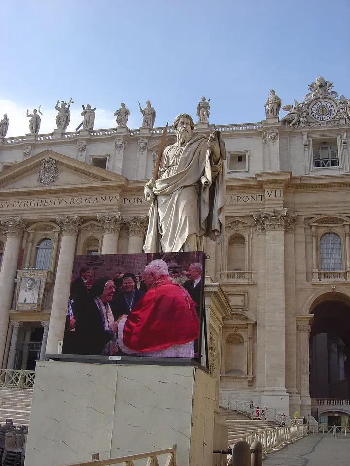 The façade of St. Peter's Basilica with the statue of St. Paul in the foreground and a large screen showing Pope Benedict XVI