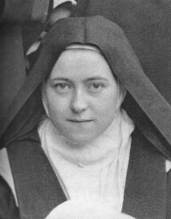 A black-and-white photograph of St. Thérèse of Lisieux as a young Carmelite nun in a dark veil and white wimple, looking calmly at the camera