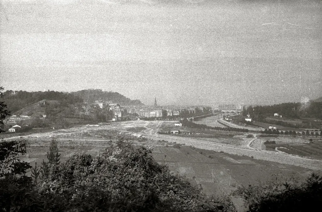 A black-and-white photograph of San Sebastián in 1941, seen from a hill, with open ground and a river valley in front of the town