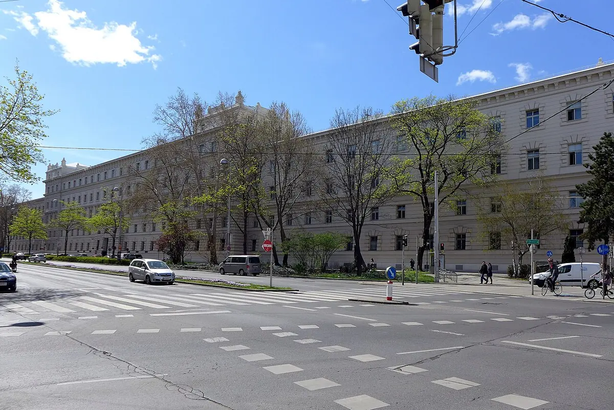 A long, plain, pale four-story court building behind spring trees across a wide city street