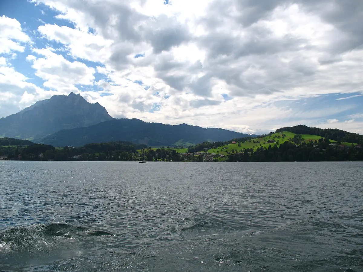 Wide gray-green lake under a cloudy sky with a dark mountain rising on the far shore