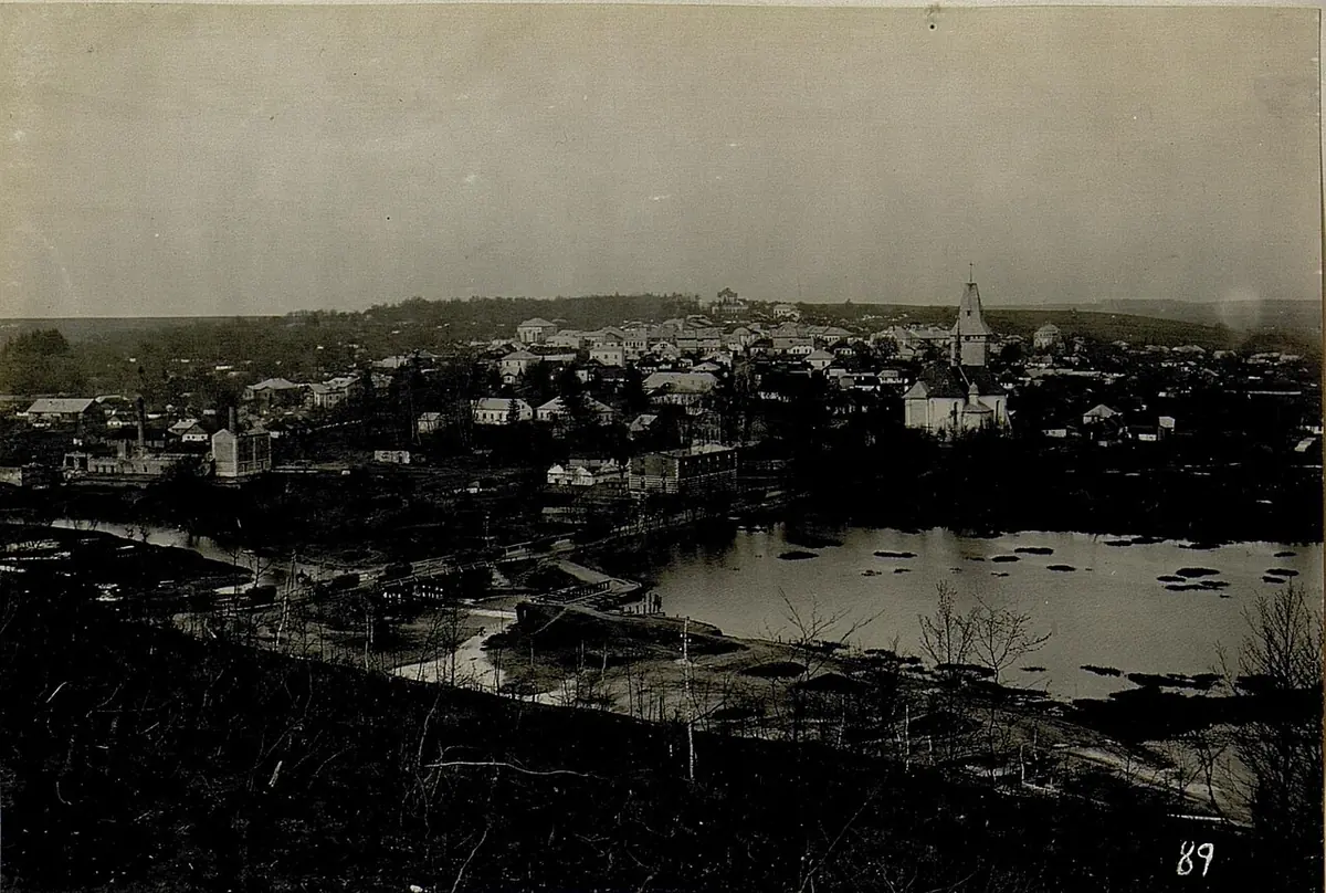 Old black-and-white photograph of a small Galician town spread along a hillside above a large pond