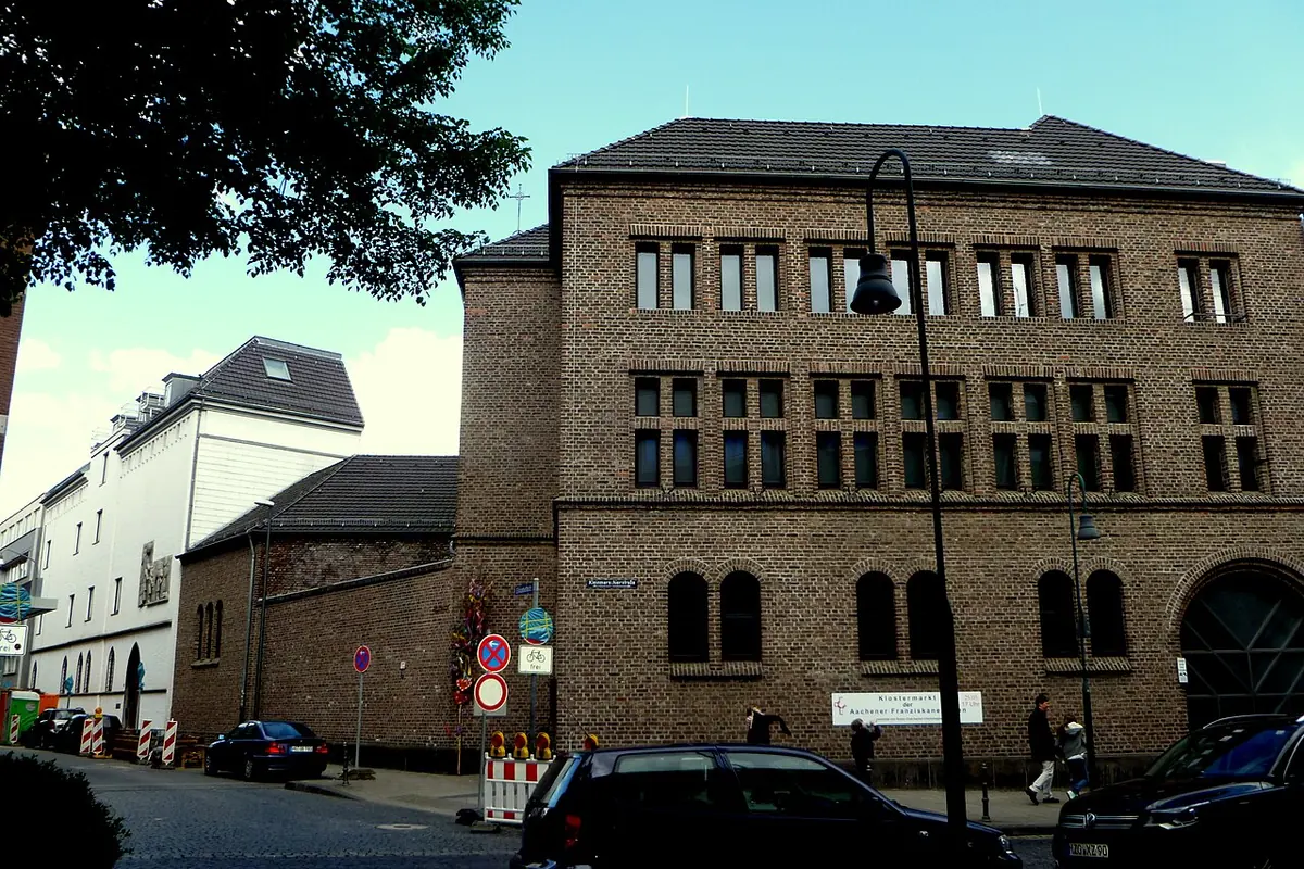 A large brown-brick convent building with rows of tall windows on a city street corner, with parked cars in front
