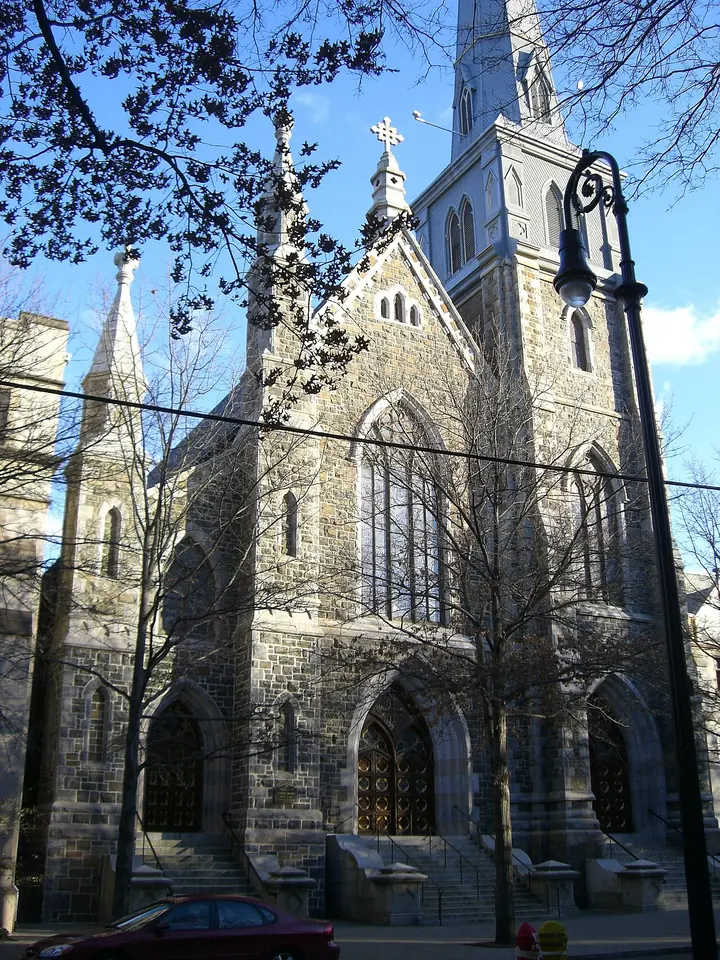 The gray stone Gothic front of St. Mary's Church in New Haven with its tall spire, seen through bare branches against a blue sky