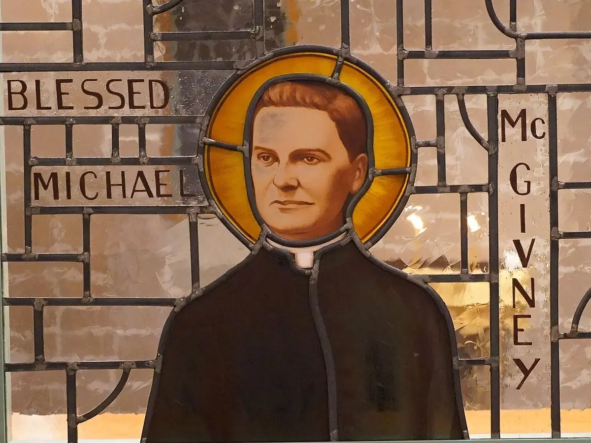 Stained-glass window of a priest in a black cassock and white collar with a golden halo, with the words Blessed Michael McGivney