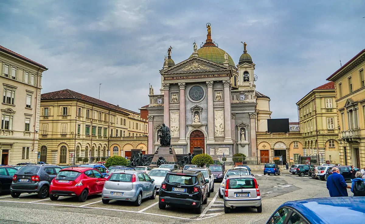 Pale stone basilica with a columned front, two bell towers and a large dome topped by a golden statue, under a blue sky