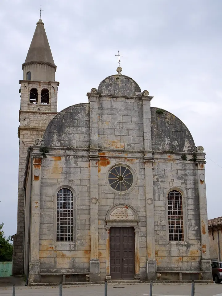The gray stone facade of the Renaissance parish church of Svetvinčenat with a rounded triple top and a tall bell tower beside it