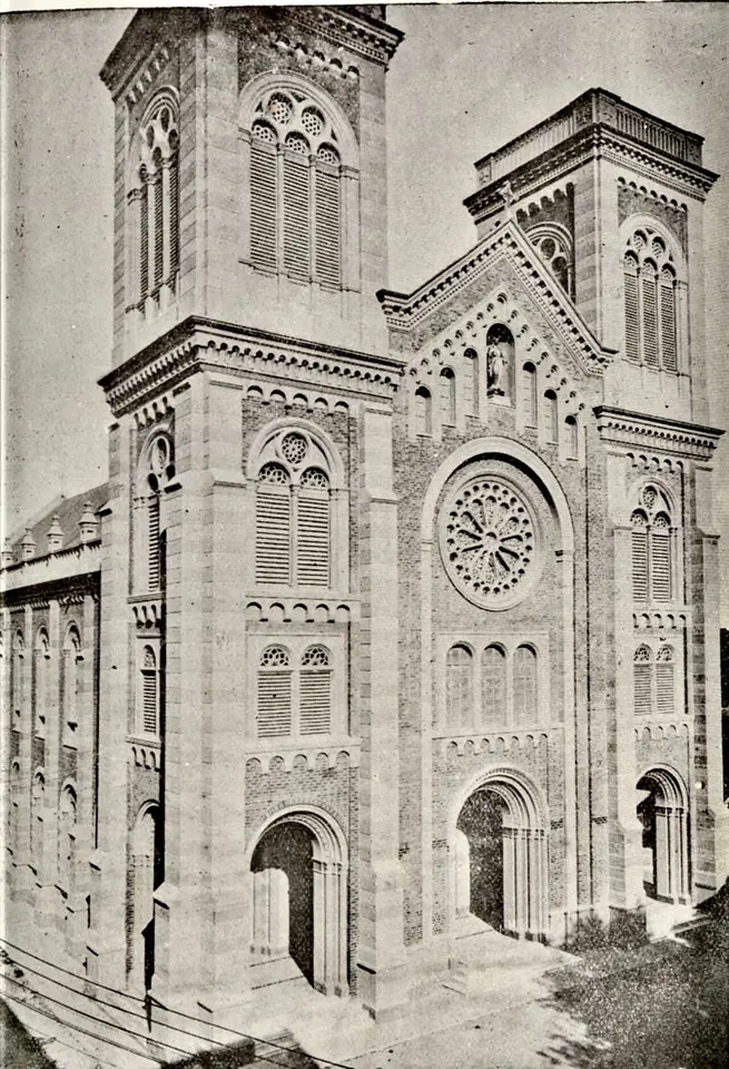 Old photograph of a tall brick church with two square bell towers, round-arched windows and a rose window over the entrance
