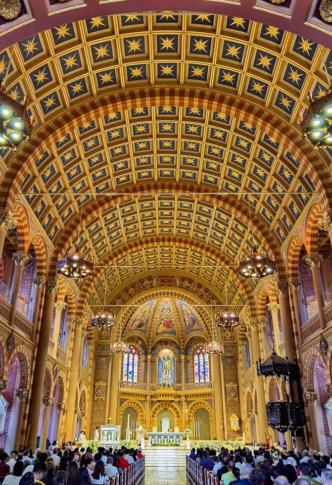 Long nave of a cathedral with a coffered golden ceiling, chandeliers and a bright sanctuary, with a congregation filling the pews