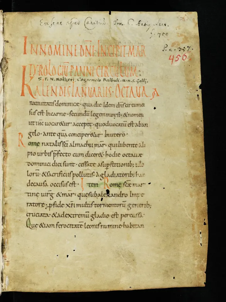 The worn first page of a medieval manuscript with red capital letters and brown Latin script, the opening of a martyrology